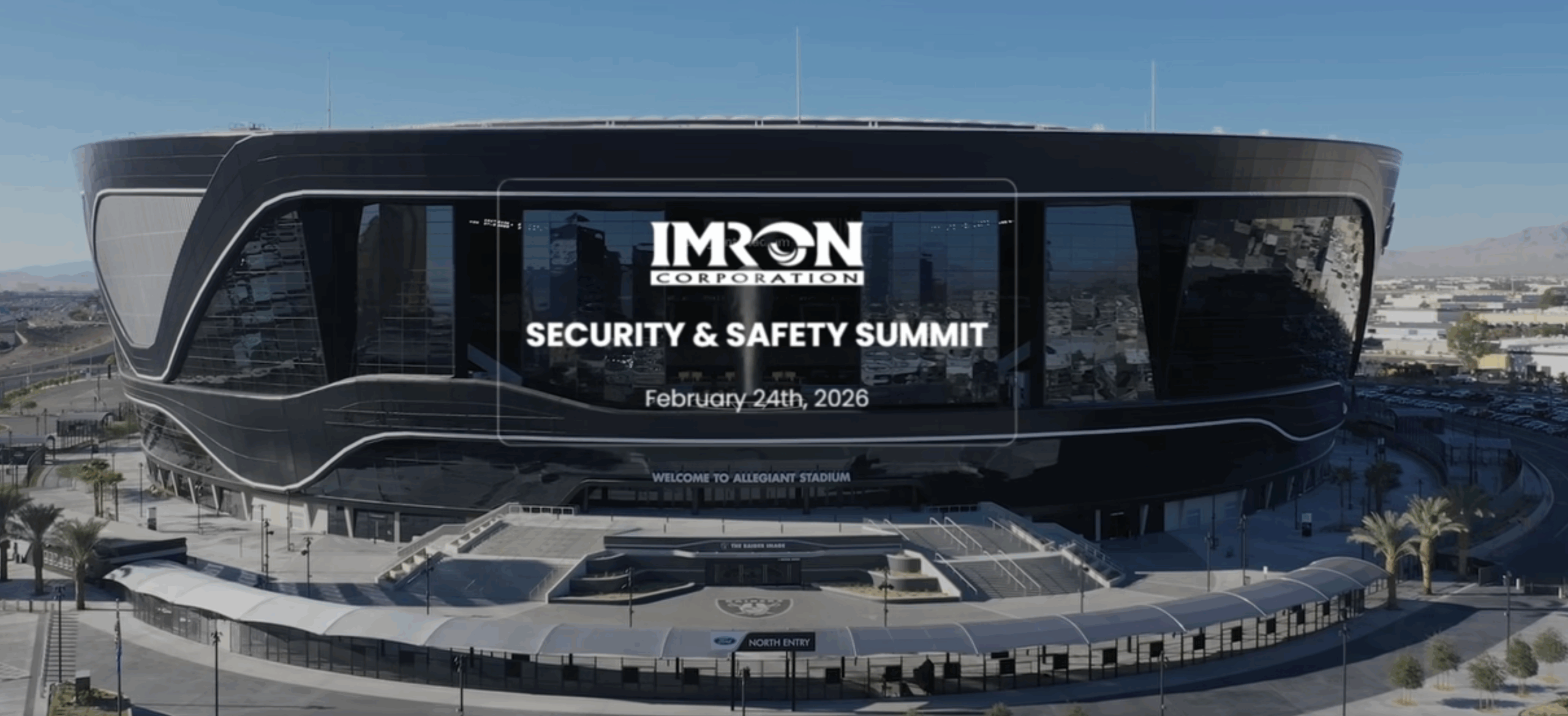 A wide aerial view of Allegiant Stadium in Las Vegas with the IMRON Corporation Security & Safety Summit graphic displayed across the front, including the event date of February 24th, 2026. The stadium’s sleek black exterior, large glass panels, and surrounding walkways are clearly visible on a bright, clear day.